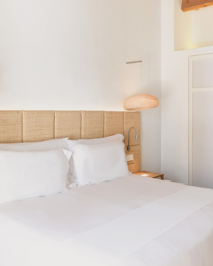 Detalle del dormitorio Garden Cottage con ropa de cama blanca, lámparas artesanales y luz natural