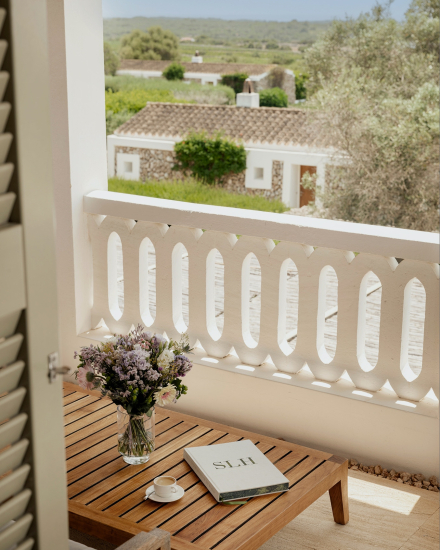 Mesa de madera con flores, taza de café y libro en una terraza con vistas al entorno rural de Torralbenc