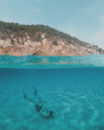Persona practicando snorkel en aguas cristalinas frente a acantilados de la costa de Menorca