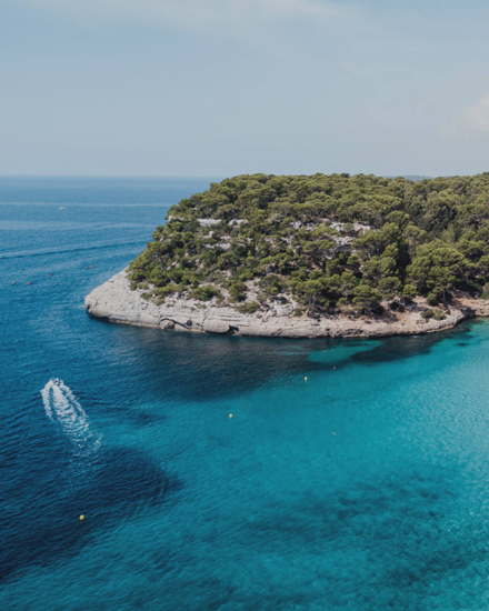 Vista aérea de una cala de aguas turquesas y acantilados cubiertos de pinos en Menorca